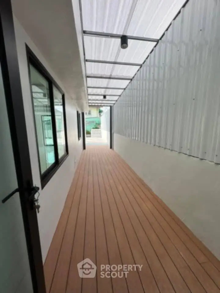 Modern covered walkway with wooden flooring and glass windows in a contemporary building.