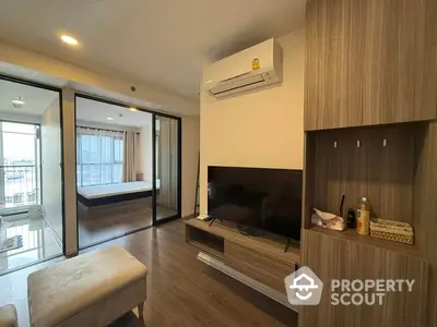 Modern living room with TV and air conditioning, open layout to bedroom, wooden flooring.