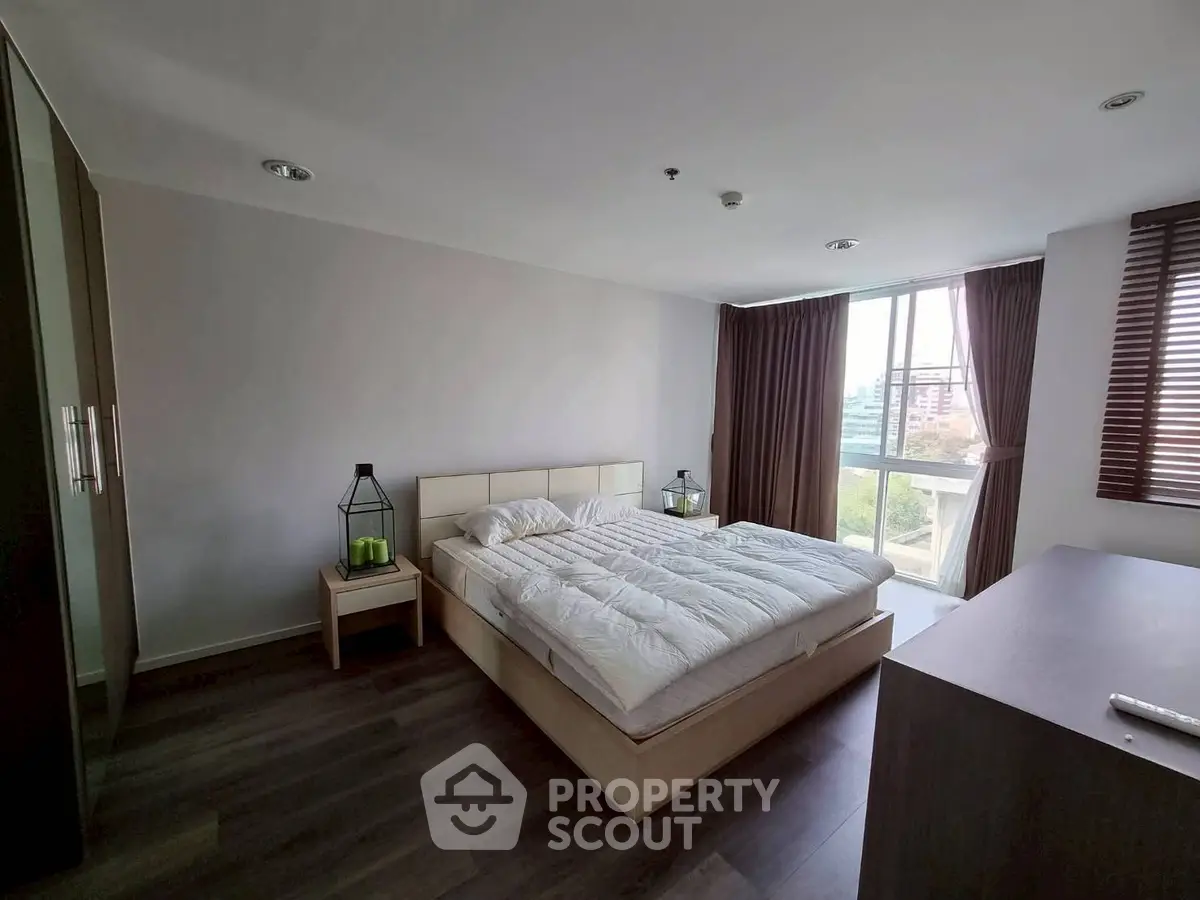 Spacious bedroom with modern decor and large window offering natural light and city view.