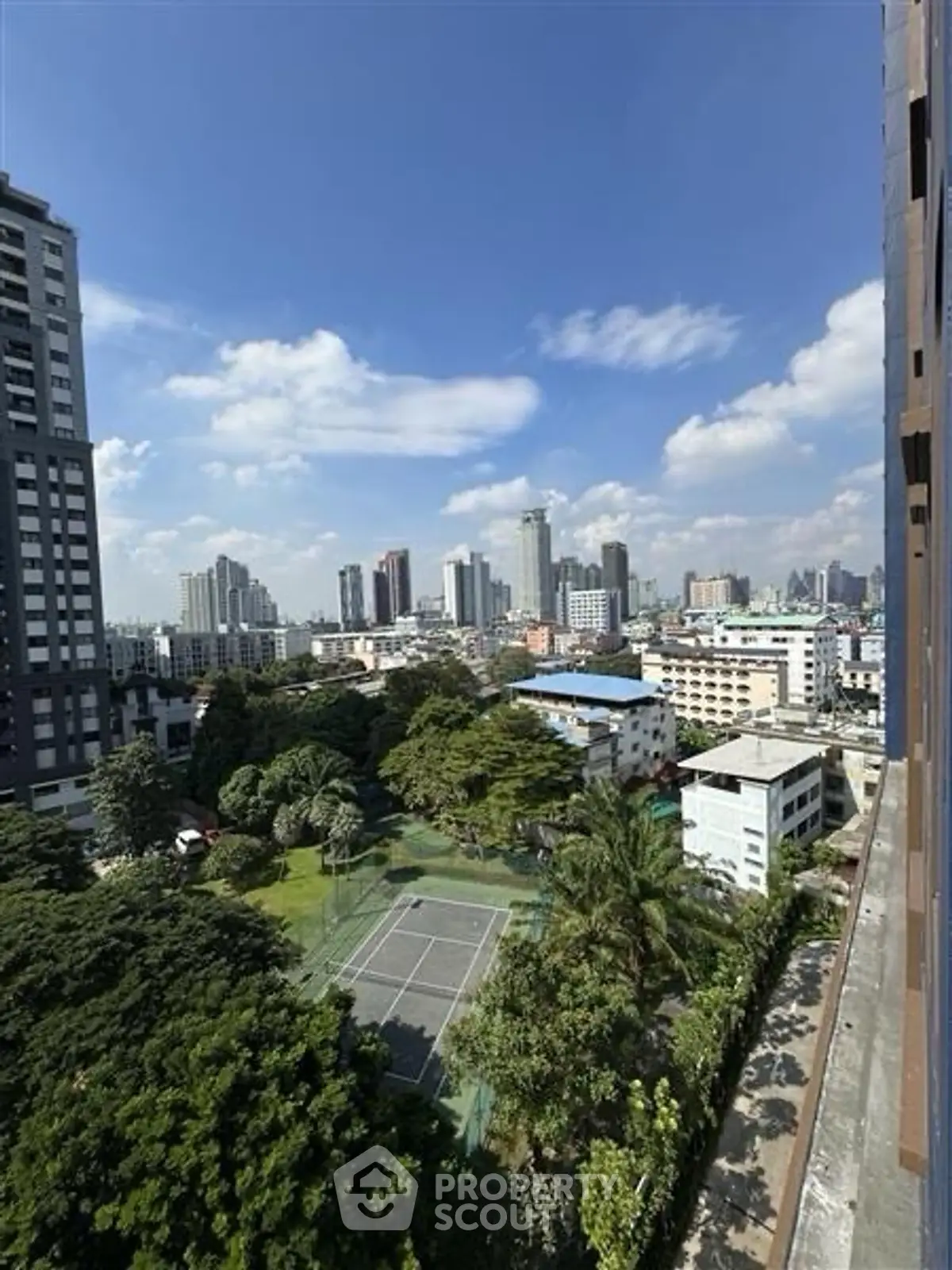 Stunning cityscape view from high-rise building with lush greenery and tennis court below.