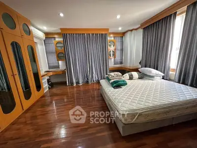 Spacious bedroom with wooden flooring and large windows for natural light.