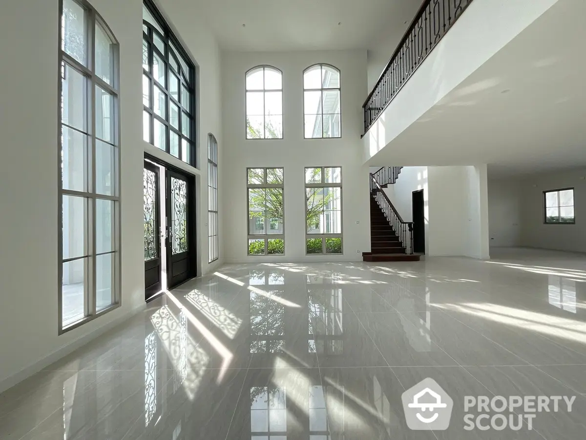 Expansive and luminous living room with soaring ceilings, grand windows, and a sleek staircase, perfect for luxurious living.