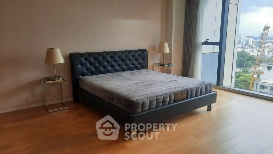 Spacious bedroom with modern bed and city view, featuring large windows and elegant decor.