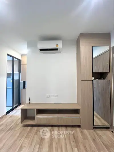 Modern living room with sleek wooden flooring and built-in storage, featuring a wall-mounted air conditioner.