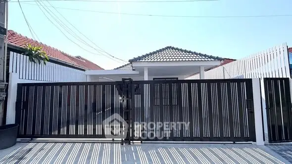 Modern house exterior with sleek black gate and tiled roof under clear blue sky.