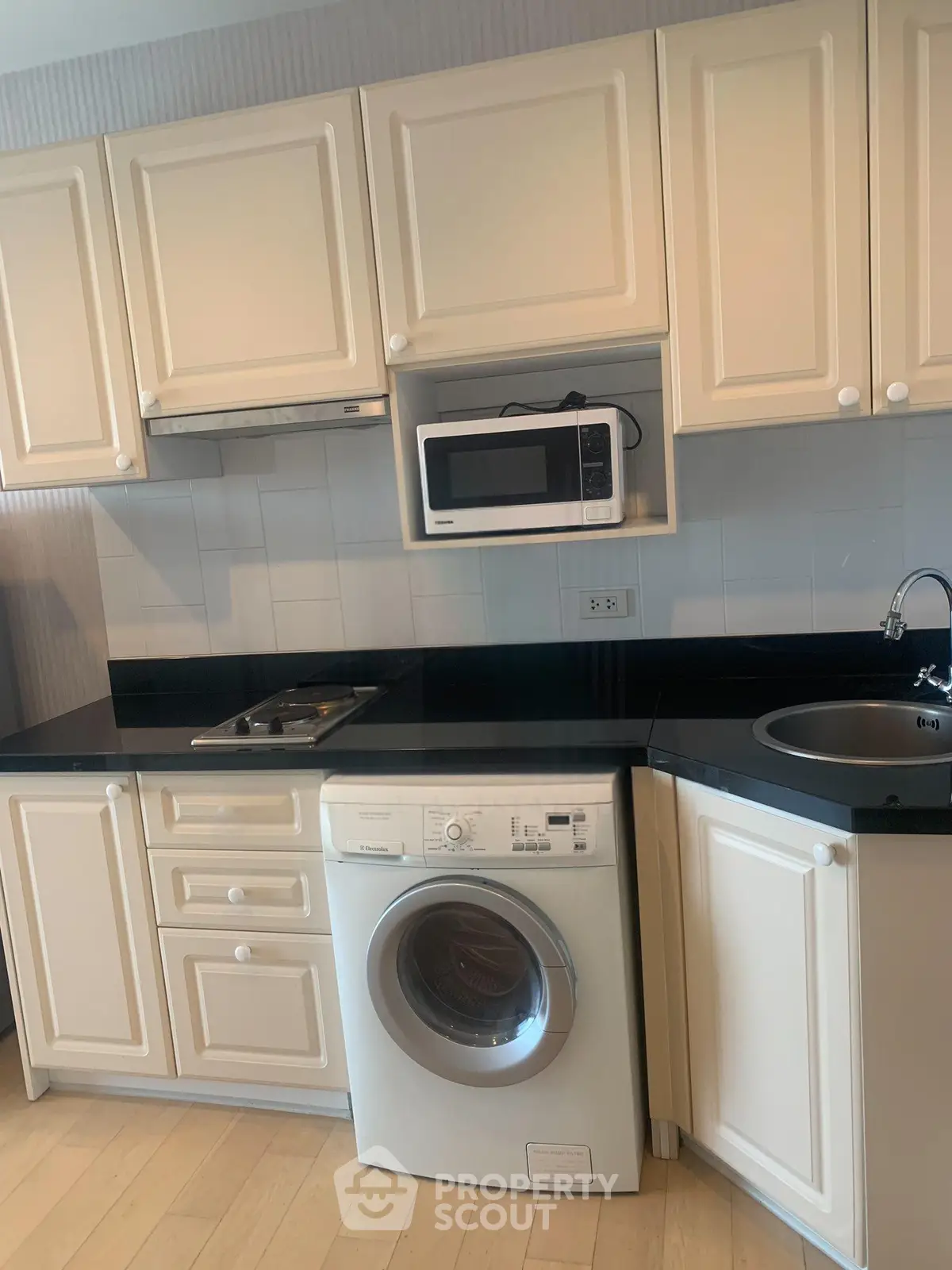 Modern kitchen with white cabinetry, built-in microwave, and washing machine under black countertop.