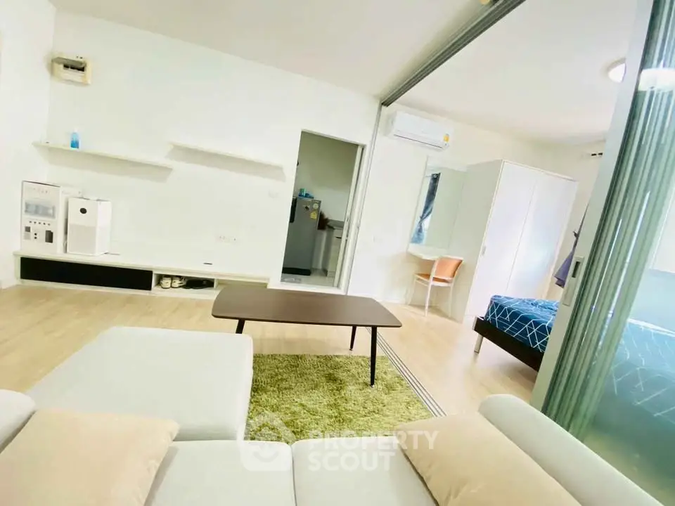 Modern open-plan living room with cozy seating and adjacent bedroom in stylish apartment.