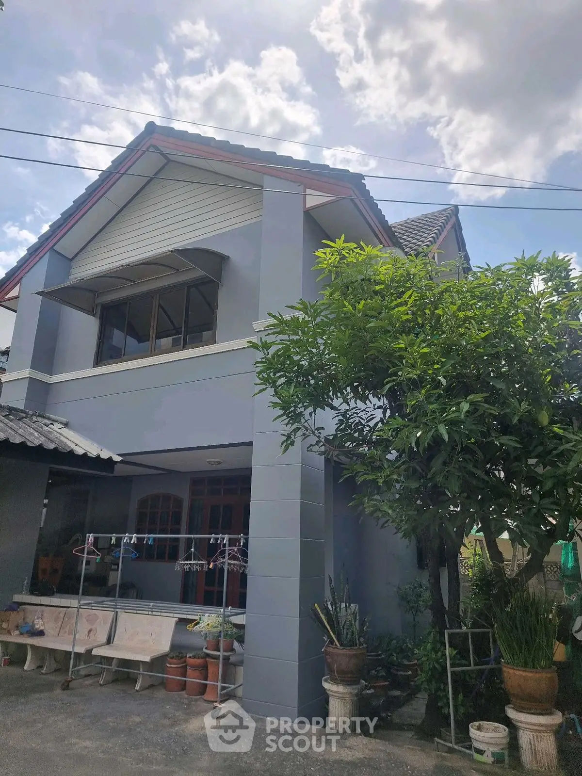 Charming two-story house with lush garden and spacious outdoor area under a bright blue sky.