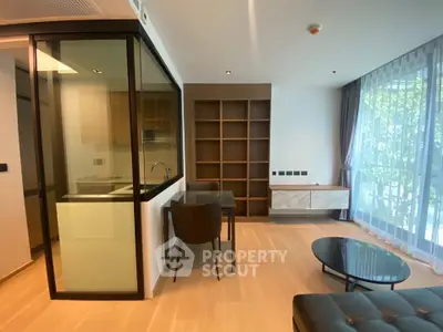 Modern living room with open kitchen and large window, featuring sleek furniture and natural light.