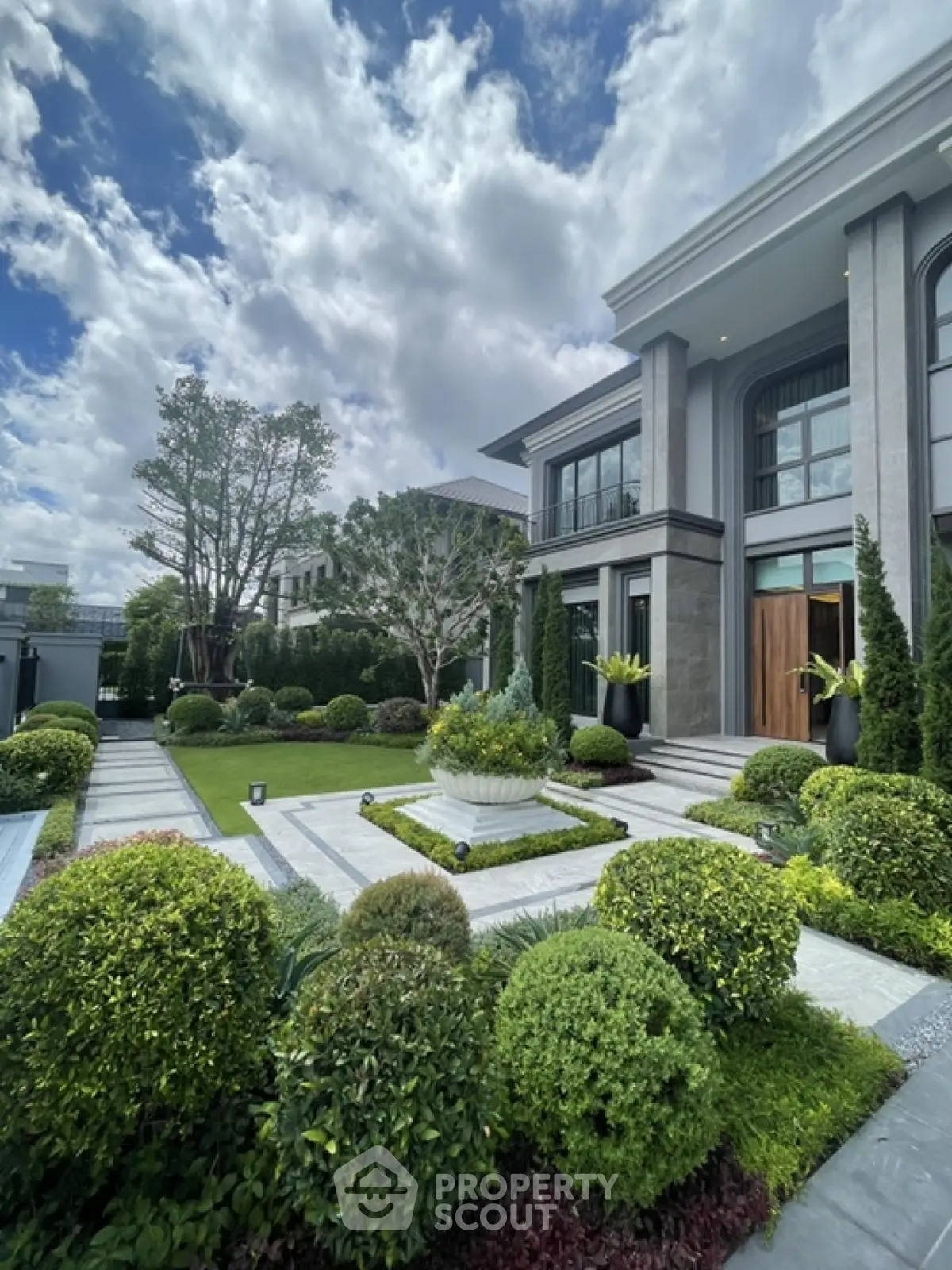 Luxurious modern mansion with manicured garden and grand entrance under a vibrant sky.