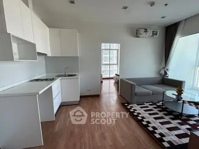 Modern open-layout living room with kitchen, featuring sleek white cabinets and cozy gray sofa.