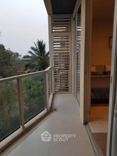 Spacious balcony with serene garden view and modern glass railing.