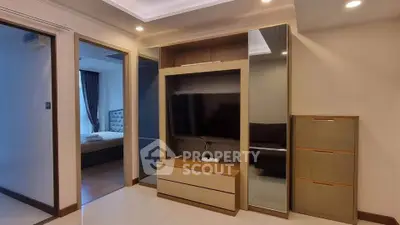 Modern living room with sleek TV unit and mirrored storage, adjacent to a cozy bedroom.