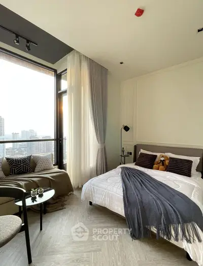 Modern bedroom with large windows and city view, featuring cozy decor and stylish furnishings.