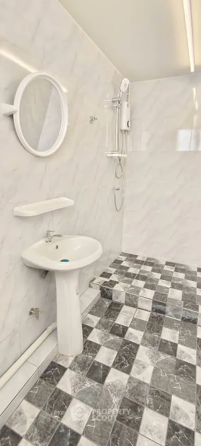 Modern bathroom with marble tiles and sleek fixtures, featuring a round mirror and shower area.
