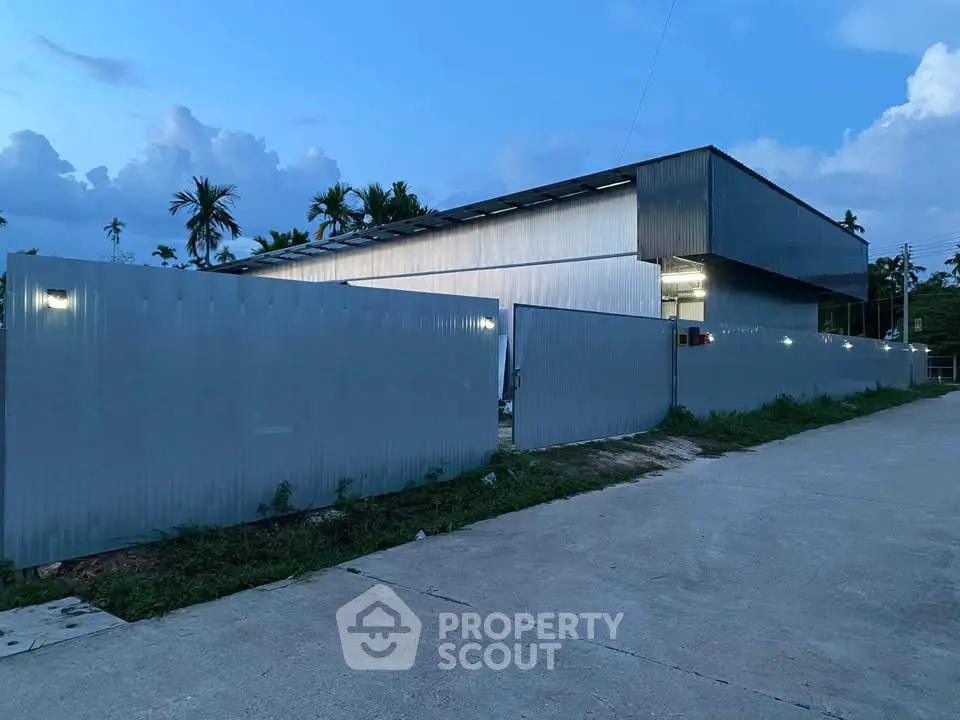 Modern industrial-style building with sleek metal facade and secure gated entrance at dusk.