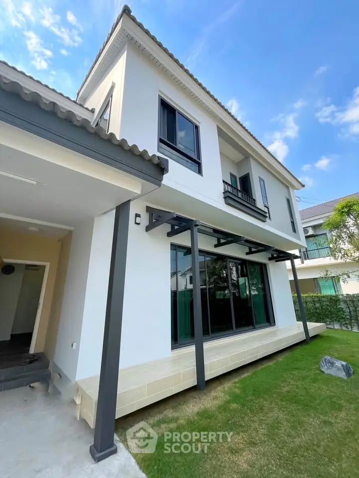 Modern two-story house with large windows and a well-maintained lawn, showcasing contemporary architecture.