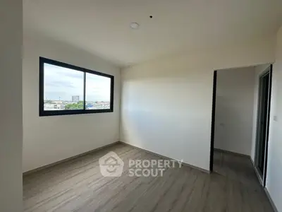 Spacious empty room with large window and wooden flooring, perfect for customization.