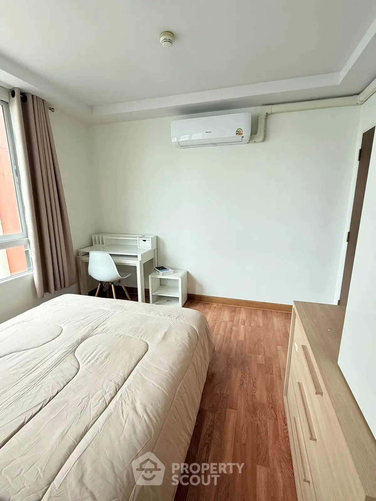 Cozy bedroom with wooden flooring, modern air conditioning, and a study desk by the window.