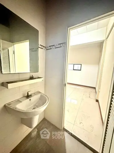 Bright bathroom with modern sink and mirror, leading to a sunlit room with tiled flooring.
