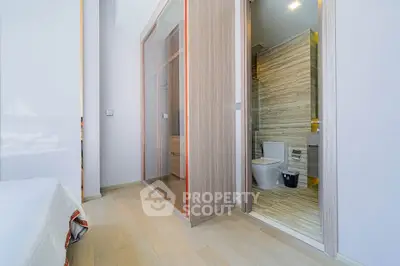 Modern bedroom with ensuite bathroom featuring sleek wooden flooring and glass wardrobe doors.