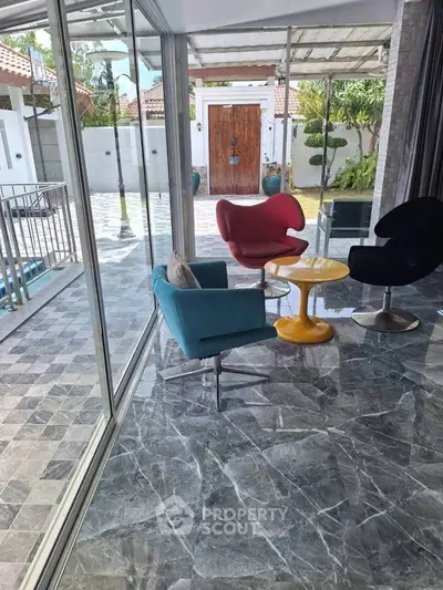 Stylish modern living area with vibrant chairs and marble flooring overlooking a spacious patio.