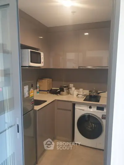 Modern compact kitchen with appliances including washing machine and microwave, sleek cabinetry, and neutral tones.