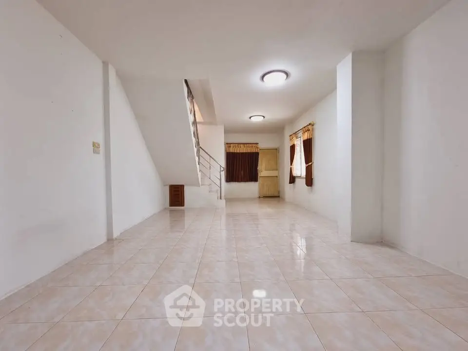 Spacious unfurnished living room with tiled flooring and staircase, ideal for customization.