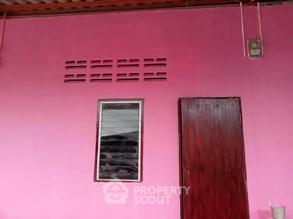 Vibrant pink exterior wall with wooden door and window, perfect for unique home design.