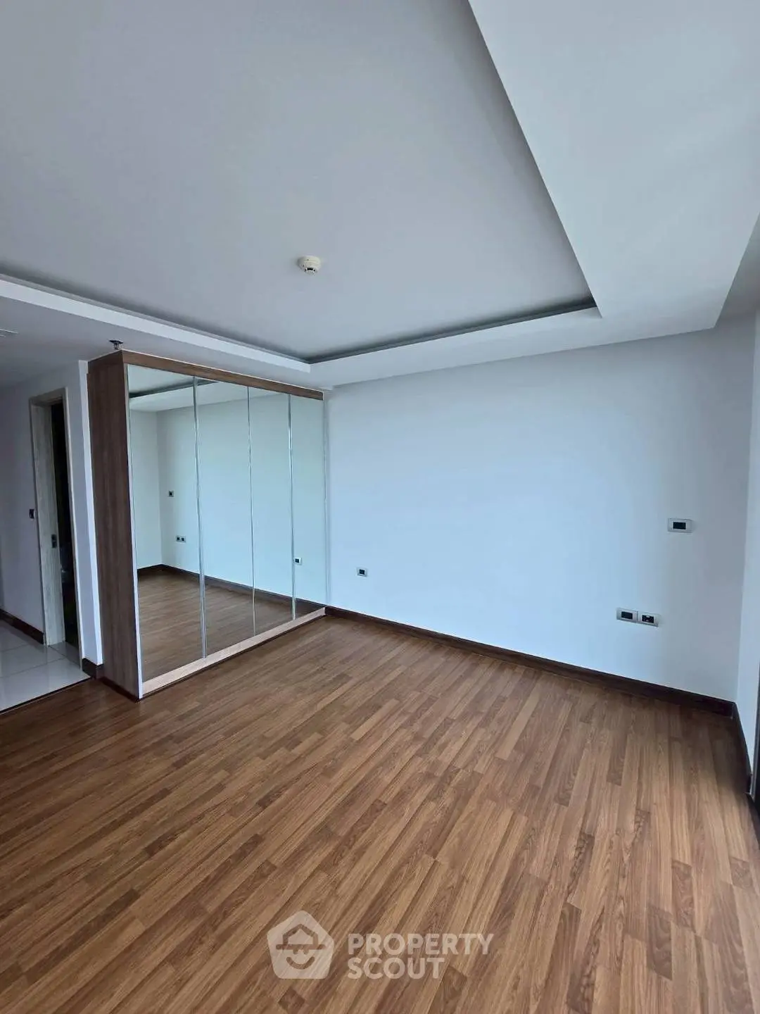 Spacious empty bedroom with wooden flooring and mirrored wardrobe
