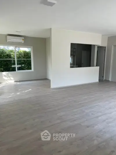 Spacious open-plan living room with large window and modern flooring, perfect for natural light and comfort.