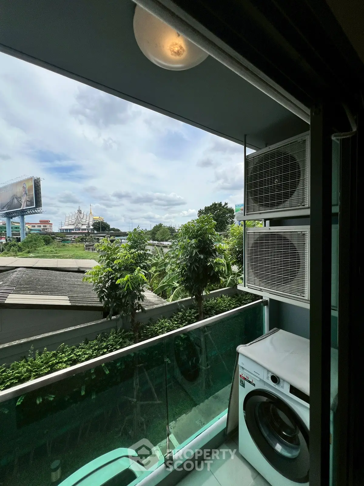 Charming balcony with lush greenery and city view, featuring modern washing machine.