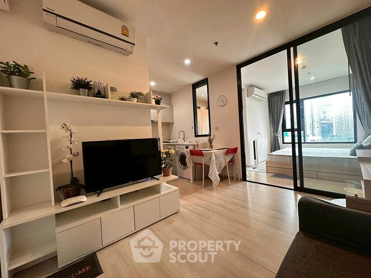 Modern open-plan living room with TV, dining area, and bedroom view in stylish apartment.