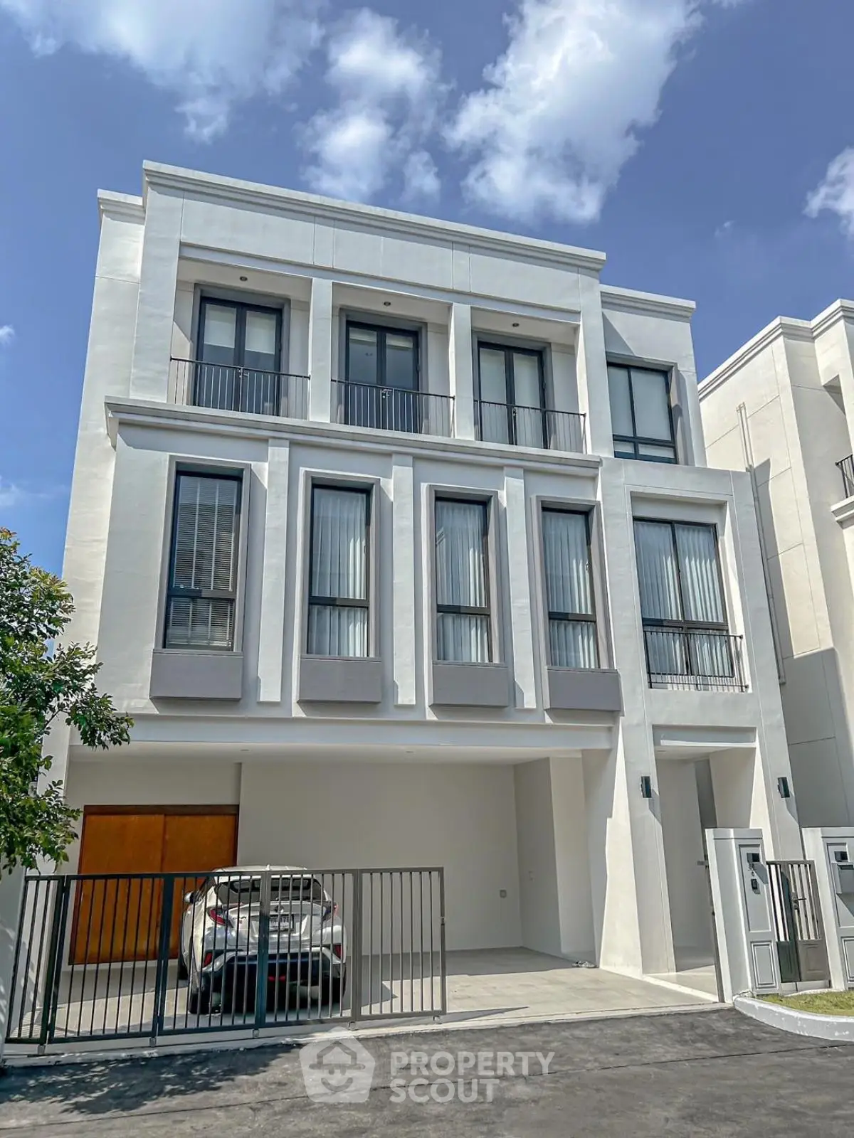 Modern three-story townhouse with sleek design and gated parking under a clear blue sky.