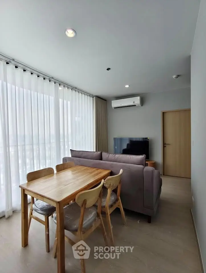 Modern living room with dining area, featuring large windows and stylish furniture.