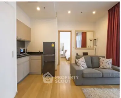 Modern living room with open kitchen, featuring sleek furniture and wooden flooring.
