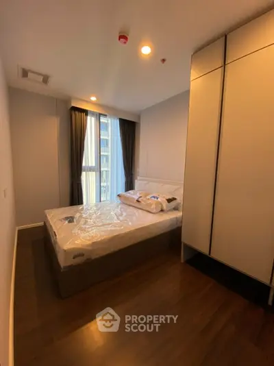 Modern bedroom with large window and sleek wardrobe in a high-rise apartment.