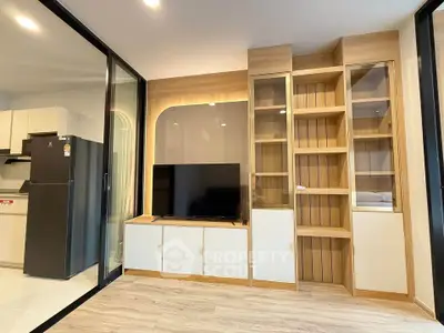 Modern living room with sleek TV unit and glass cabinets, adjacent to a stylish kitchen.