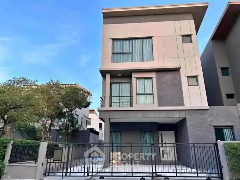 Modern three-story house with sleek design and gated entrance in a serene neighborhood.