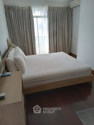 Cozy bedroom with large window and elegant curtains, featuring a comfortable bed and wooden flooring.