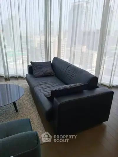 Modern living room with sleek black sofa and city view through large windows.
