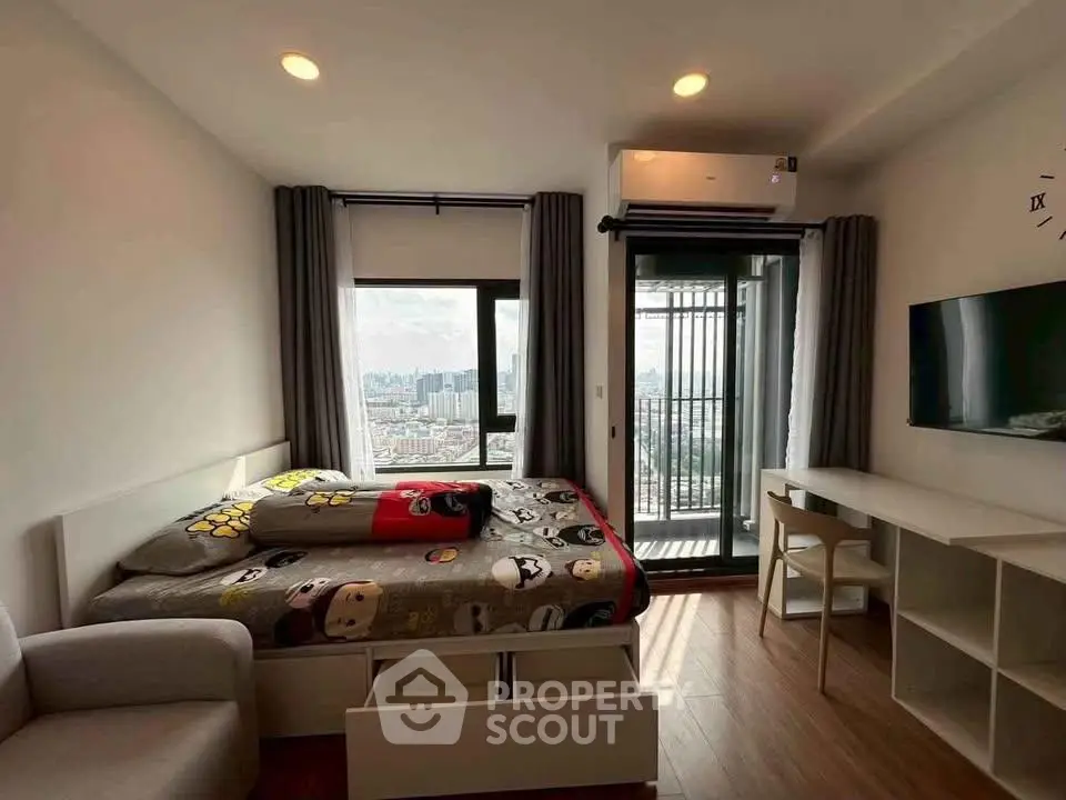 Modern bedroom with city view, featuring a cozy bed, desk, and balcony access in a high-rise apartment.