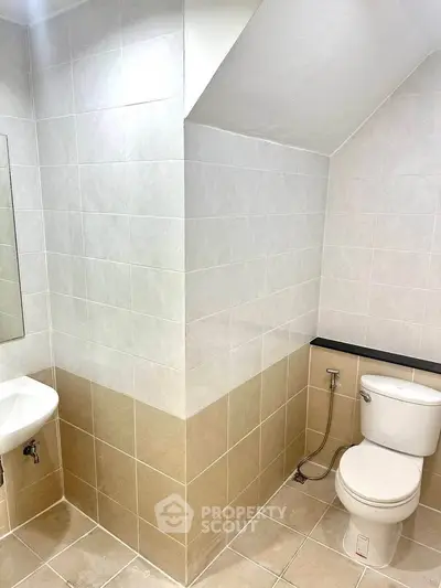 Modern bathroom with sleek tiles and compact design, featuring a toilet and sink under a sloped ceiling.