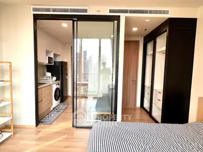 Modern studio apartment with glass partition, featuring compact kitchen and cozy bedroom area.