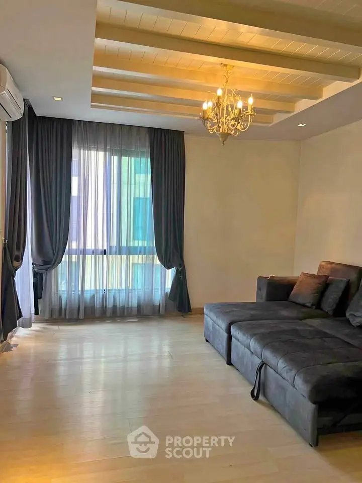 Spacious living room with elegant chandelier and large window in modern apartment.