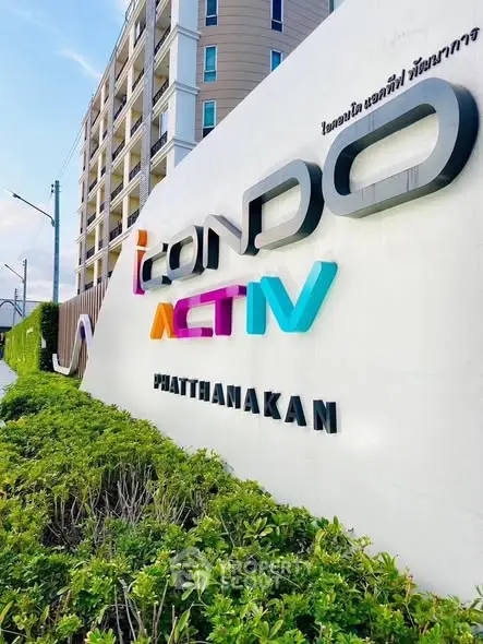 Modern condo building entrance with vibrant signage and lush greenery.