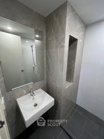 Modern bathroom with sleek sink and elegant gray tiles, featuring a minimalist design and built-in shower area.