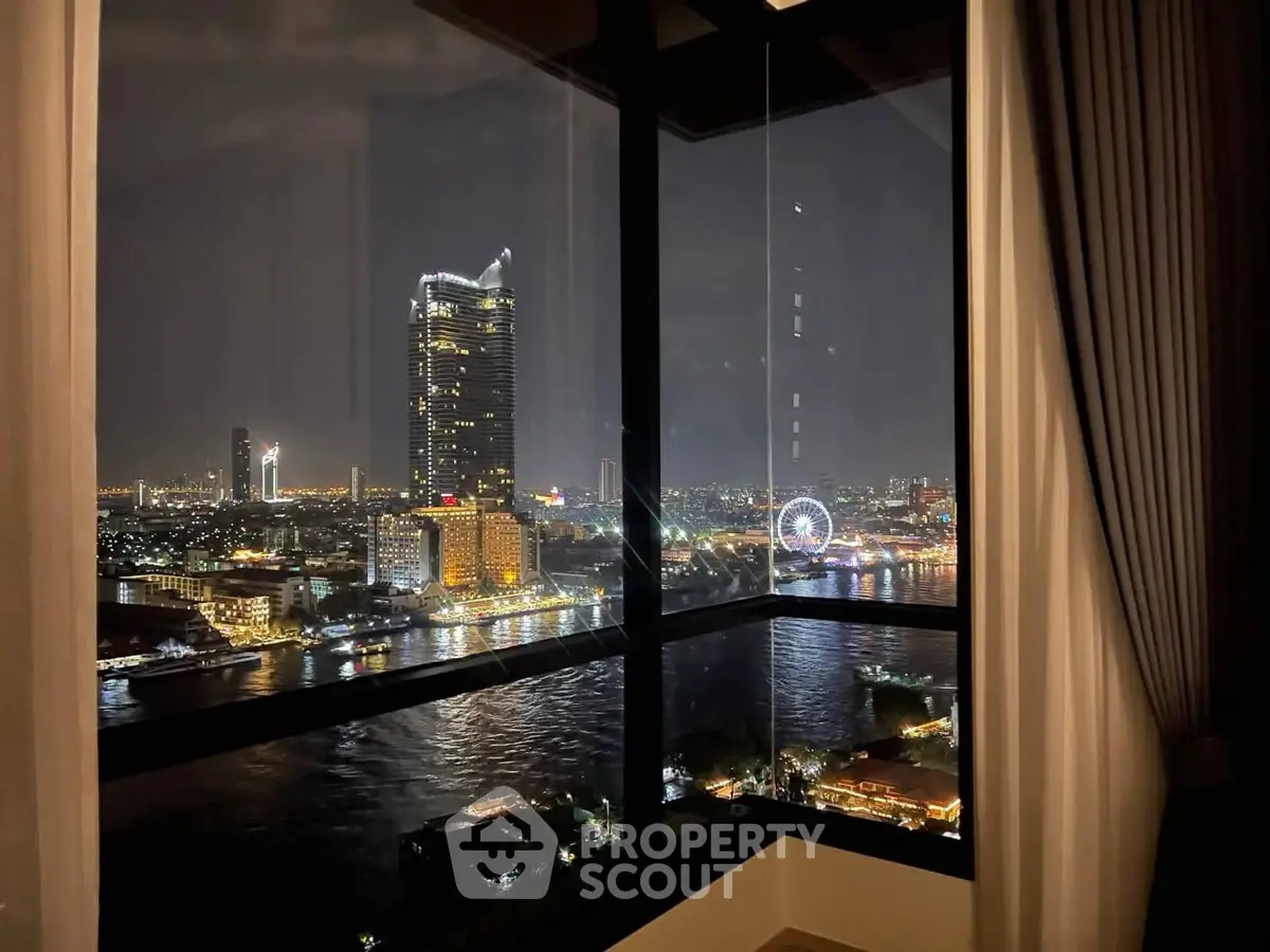 Stunning cityscape view from a high-rise apartment window at night, overlooking a river and illuminated skyline.