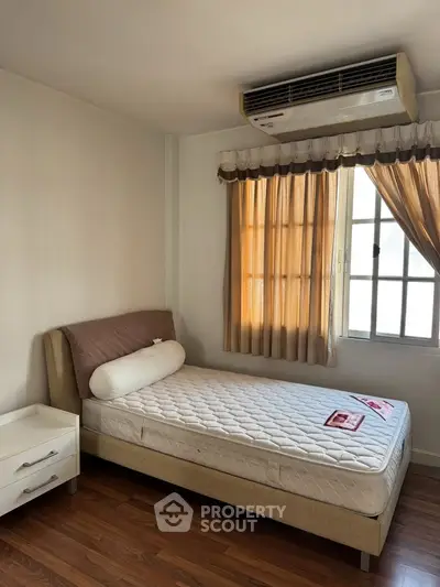 Cozy bedroom with natural light and air conditioning, featuring a comfortable bed and wooden flooring.