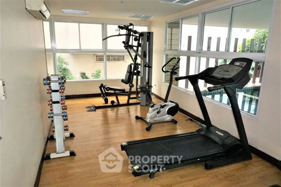 Modern gym with treadmill and exercise equipment in a bright room with large windows.